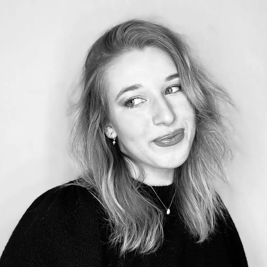 Schwarz-weiß-Porträt von Annalena, halbnah, Blick zur Seite, schulterlanges Haar, dezente Ohrringe und Kette, neutraler Hintergrund.